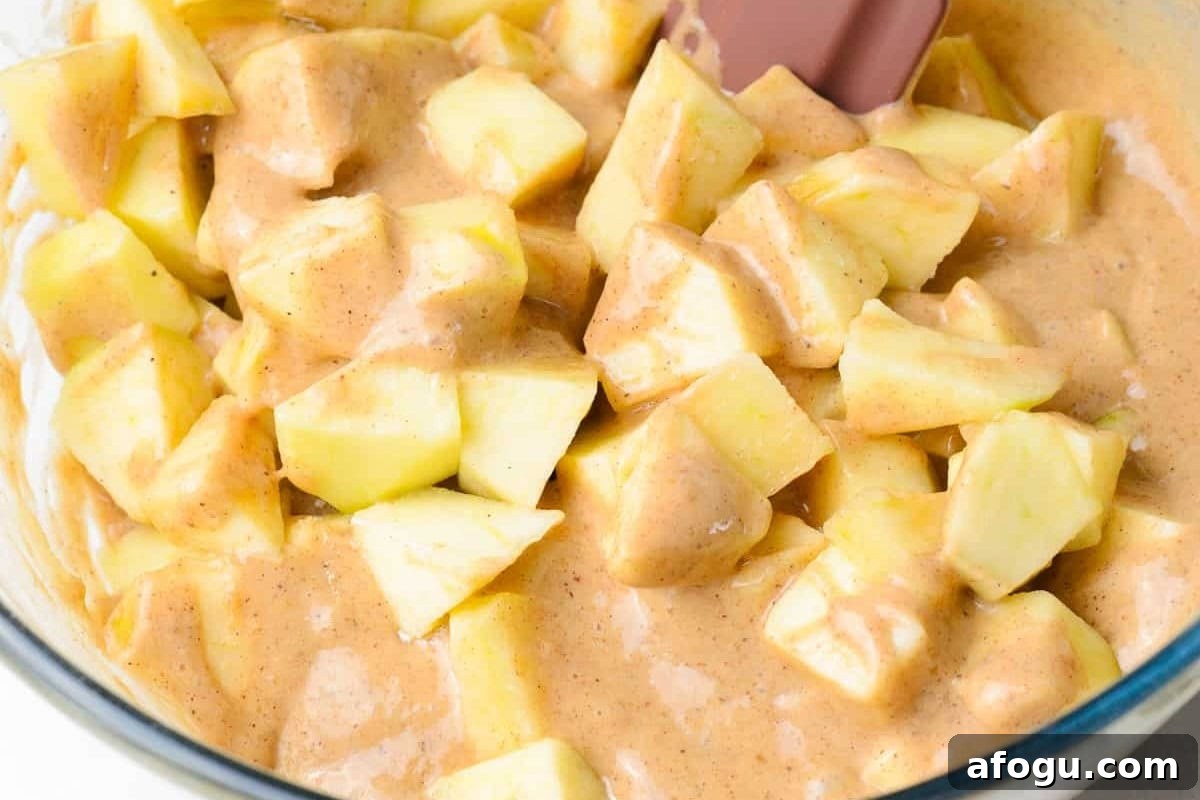folding apple chunks into batter in a glass bowl.