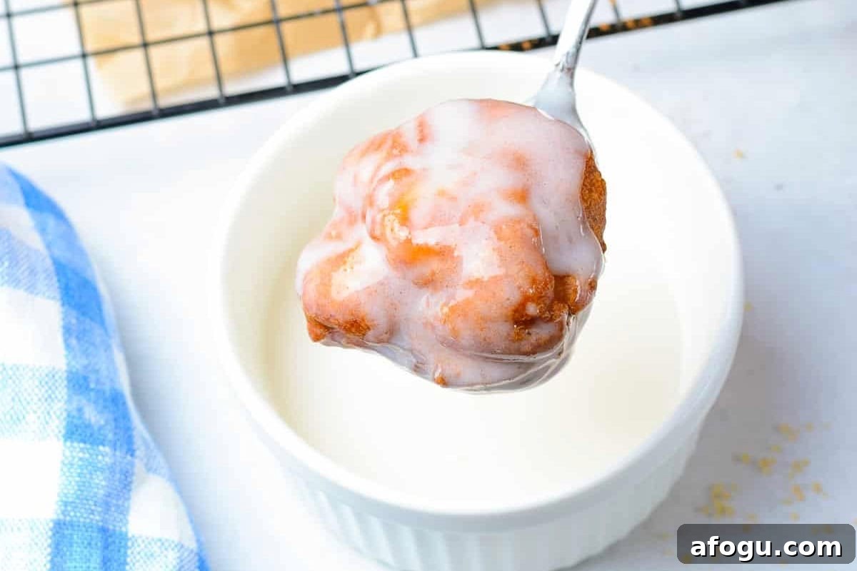 dipping a freshly fried apple fritter in white glaze with a fork.