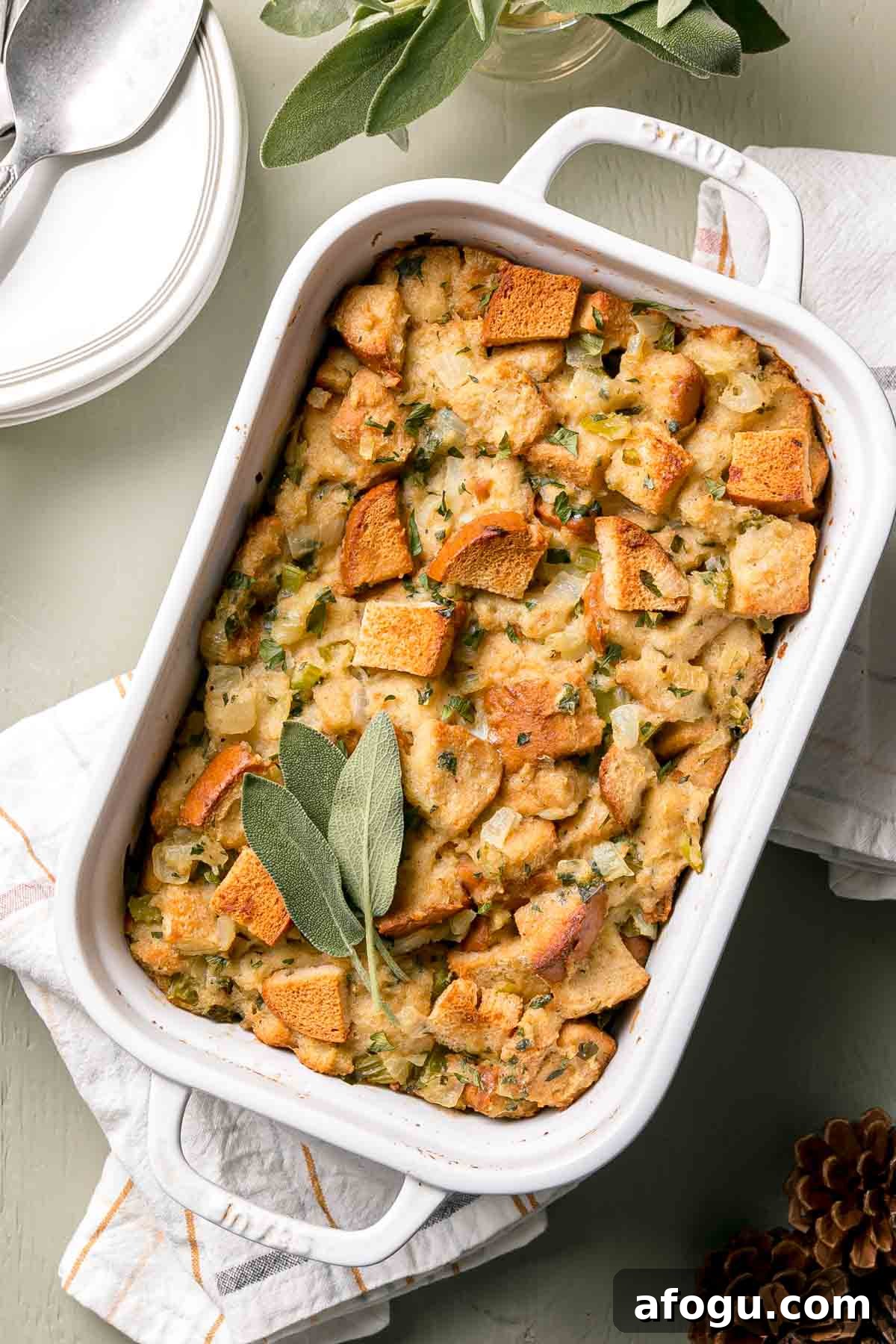White Staub casserole dish with golden brown baked stuffing and sage leaves on top.
