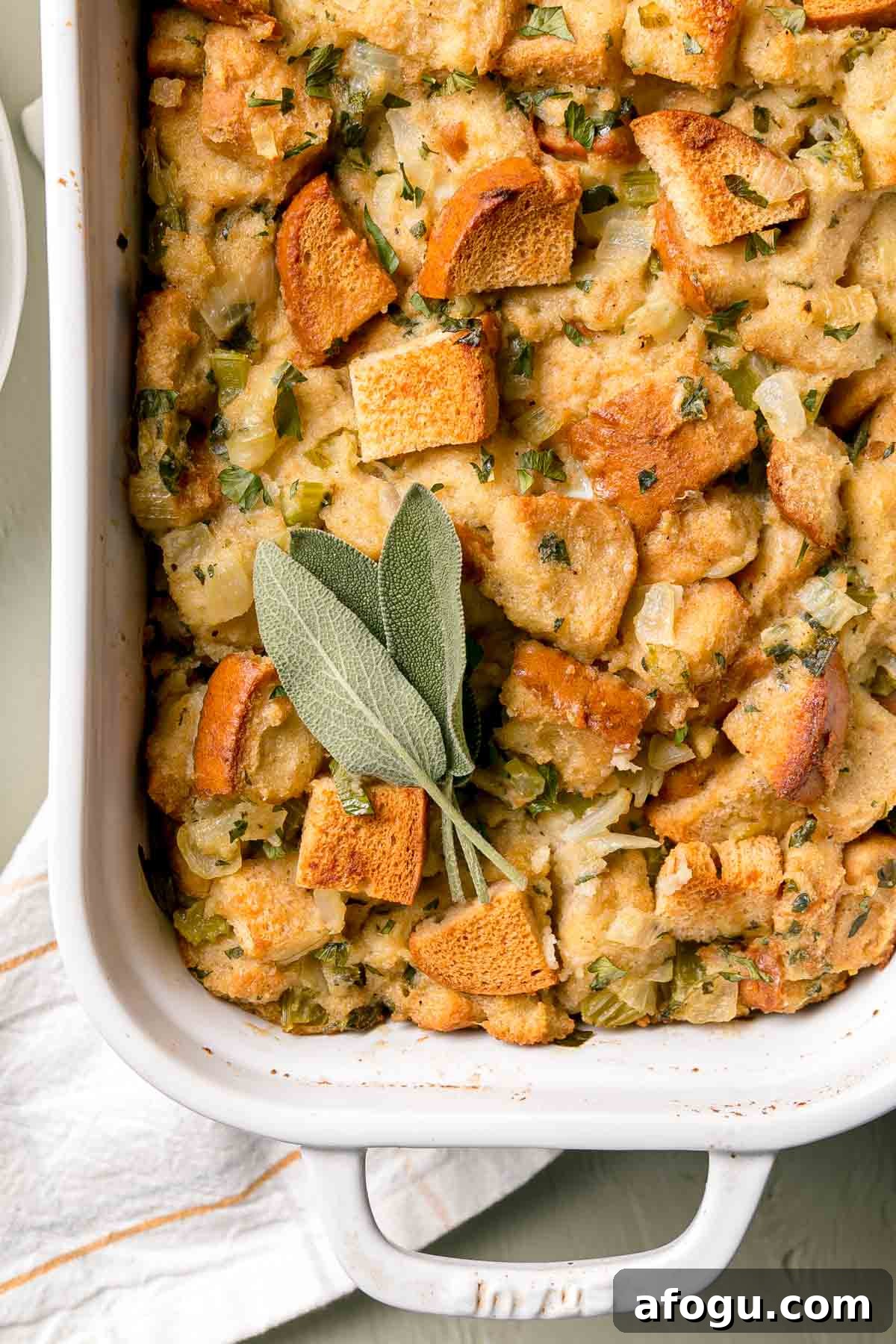 Close up image of baked stuffing showing golden brown toasted tops of bread cubes, garnished with sage leaves.