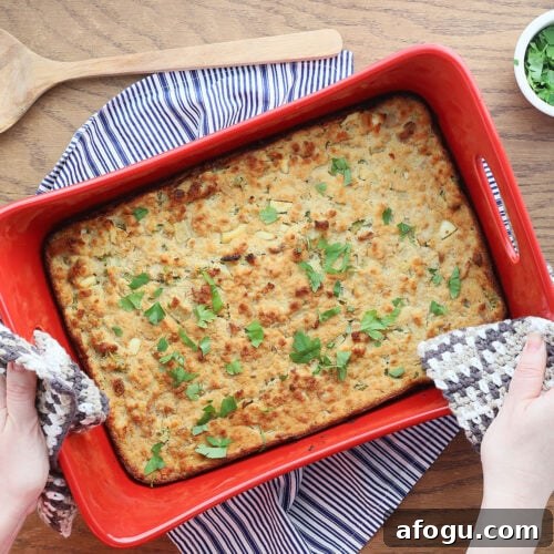 pair of hands placing a red pan of southern cornbread dressing with chicken on a table