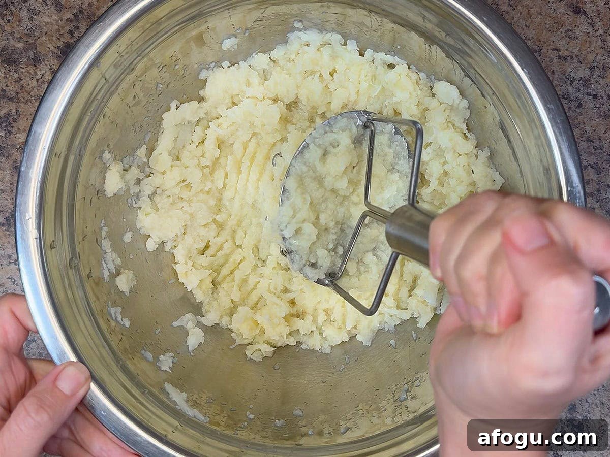 Creamy Cauliflower and Cheese Casserole Recipe 4 Using a potato masher to mash steamed cauliflower florets in a large mixing bowl.