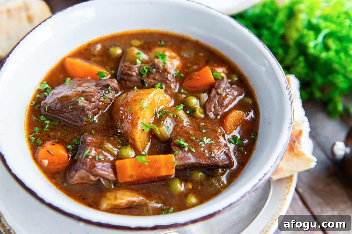 A bowl of beef stew with potatoes, carrots and peas.