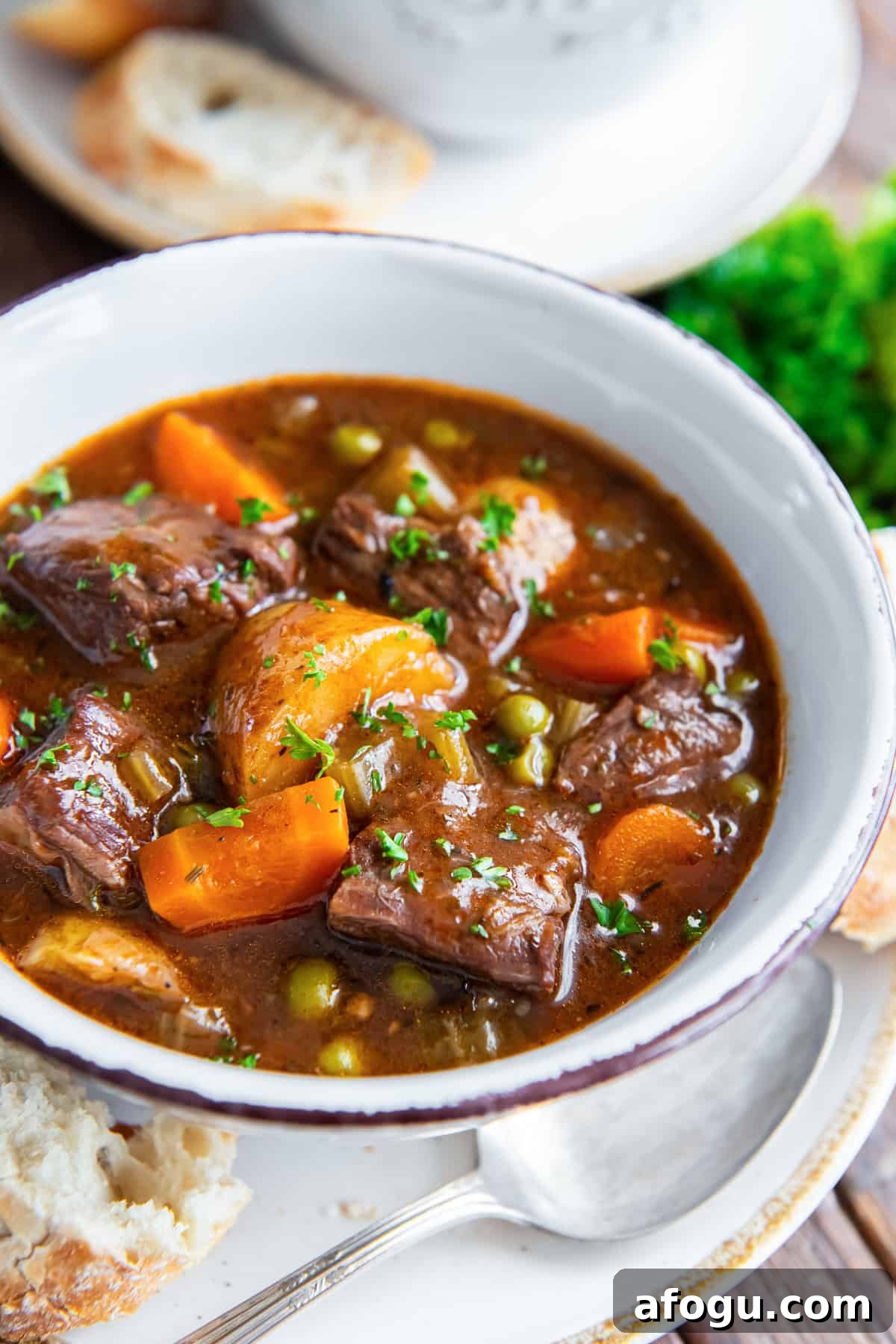 A bowl of beef stew with potatoes, carrots and peas.