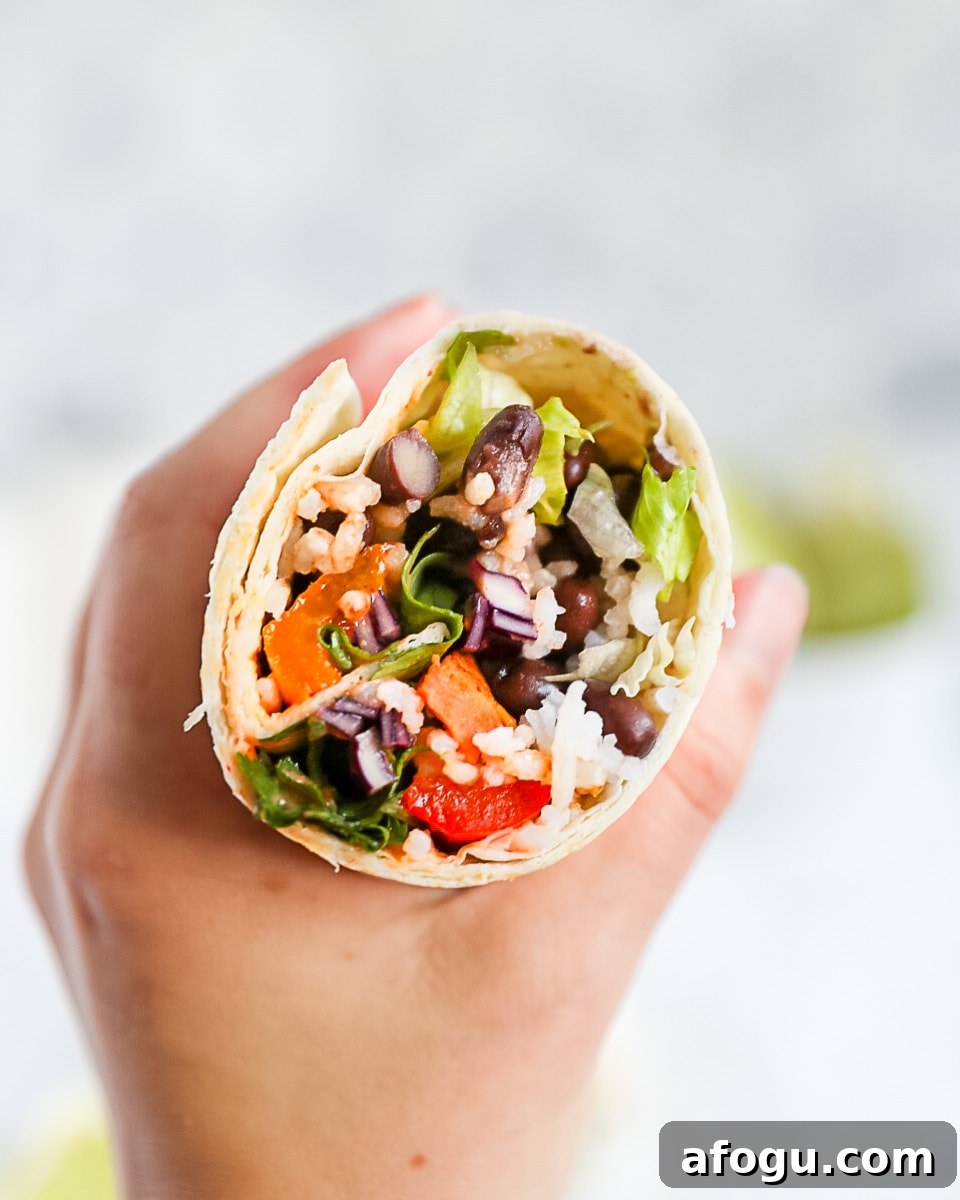 A hand holding up on half of a veggie burrito with the contents facing the camera.