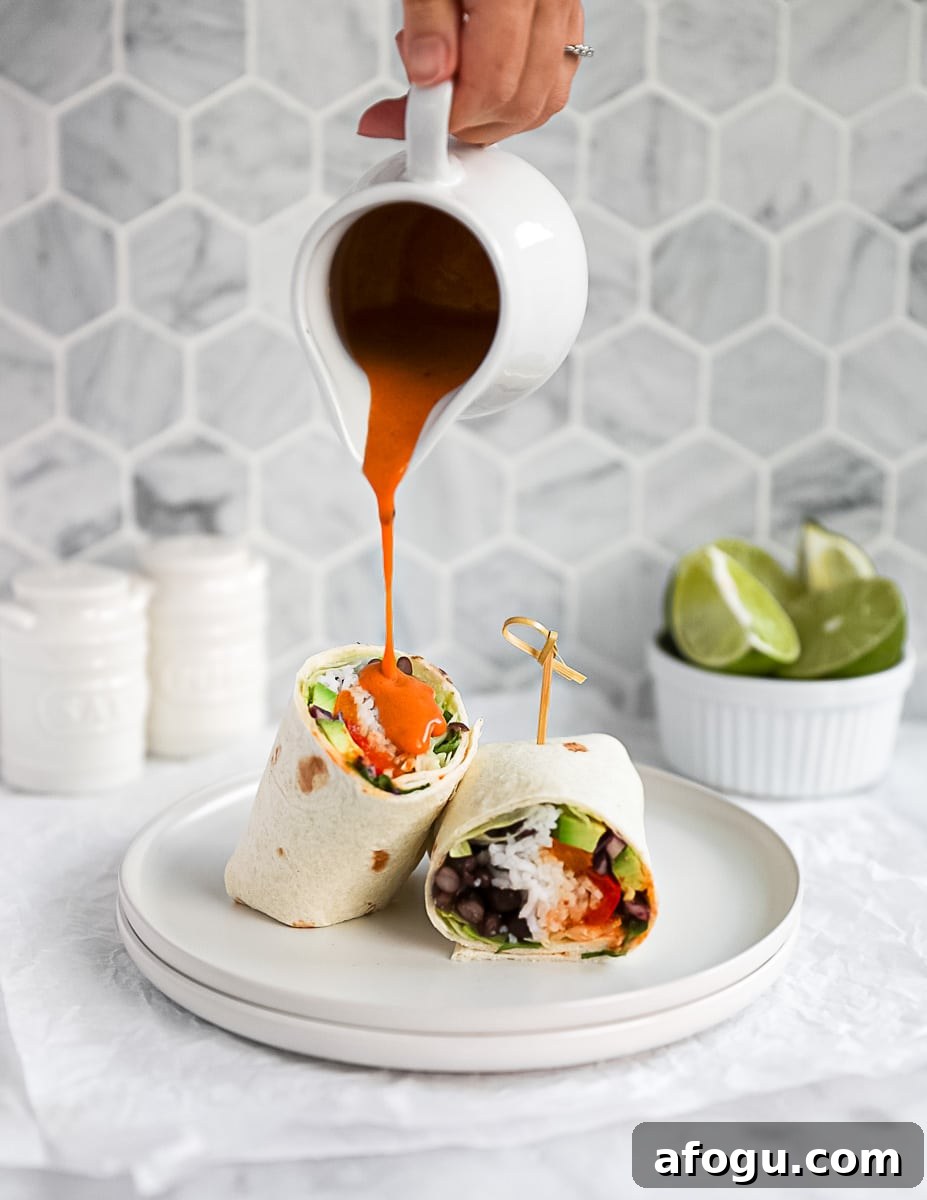 A sliced burrito with a hand pouring a container of chipotle sauce on top.
