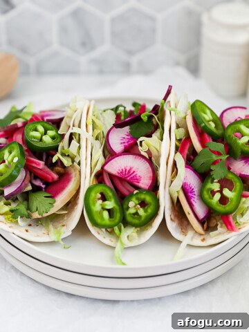 Three vegetable tacos on a stack of white plates filled with fresh vegetables.