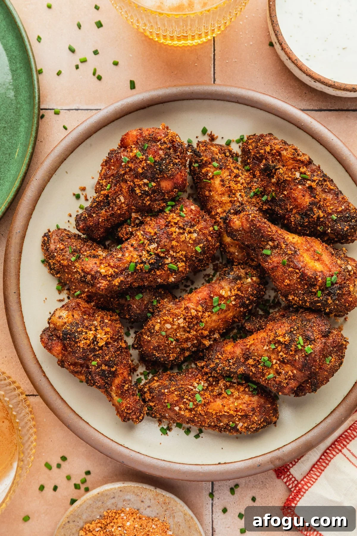 Crispy Dry-Rub Chicken Wings — Oven or Air Fryer Recipes 2 A stoneware plate of dry rub chicken wings on an orange tiled counter next to a green plate, orange striped linen, glasses of beer, and brown bowls of dry rub and ranch.