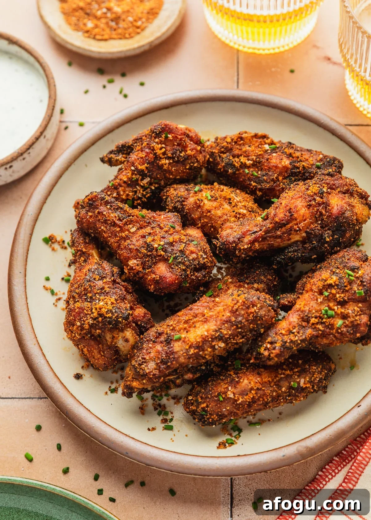 Crispy Dry-Rub Chicken Wings — Oven or Air Fryer Recipes 12 A white stoneware plate of dry rub chicken wings on an orange tiled counter next to a white bowl of ranch, glasses of beer, and orange striped linen.