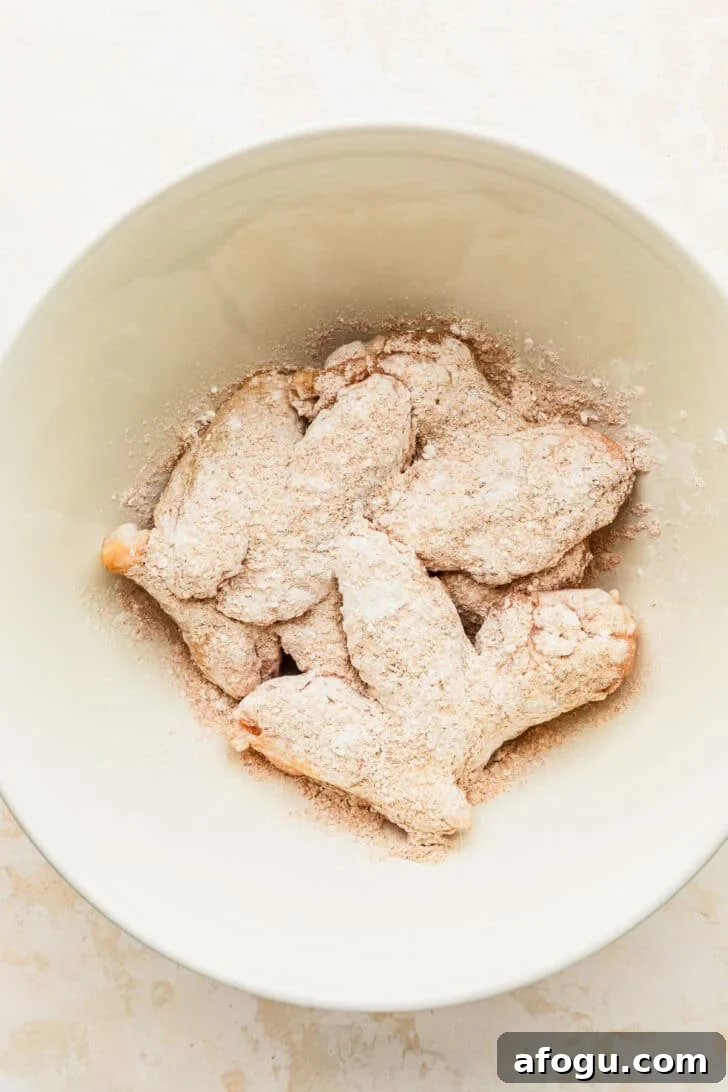 Crispy Dry-Rub Chicken Wings — Oven or Air Fryer Recipes 4 A white bowl of chicken with cornstarch on a white counter.