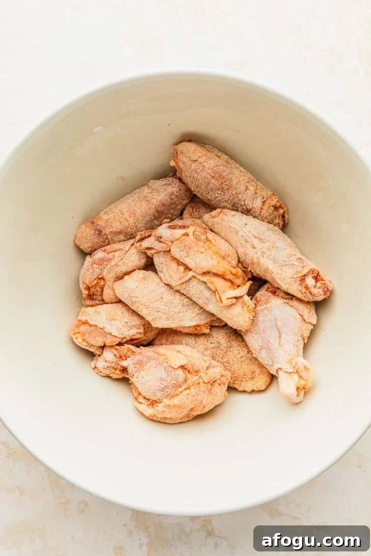 Crispy Dry-Rub Chicken Wings — Oven or Air Fryer Recipes 5 A white bowl of chicken tossed with spices on a white counter.