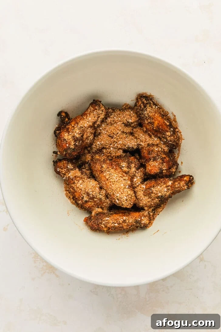 Crispy Dry-Rub Chicken Wings — Oven or Air Fryer Recipes 8 A white bowl of baked chicken wings topped with dry rub on a white counter.