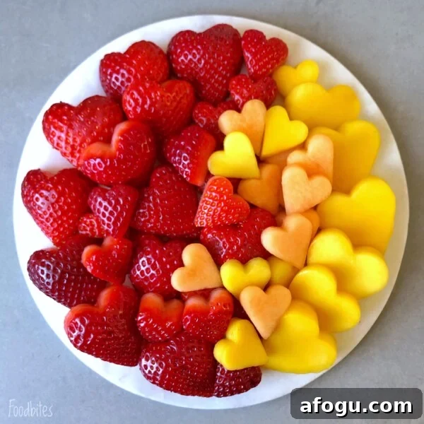 Elegant Fruit Platter Ideas for Special Occasions 3 A round white plate with heart-shaped pieces of strawberries, cantaloupe, and mango arranged by color on a gray surface.