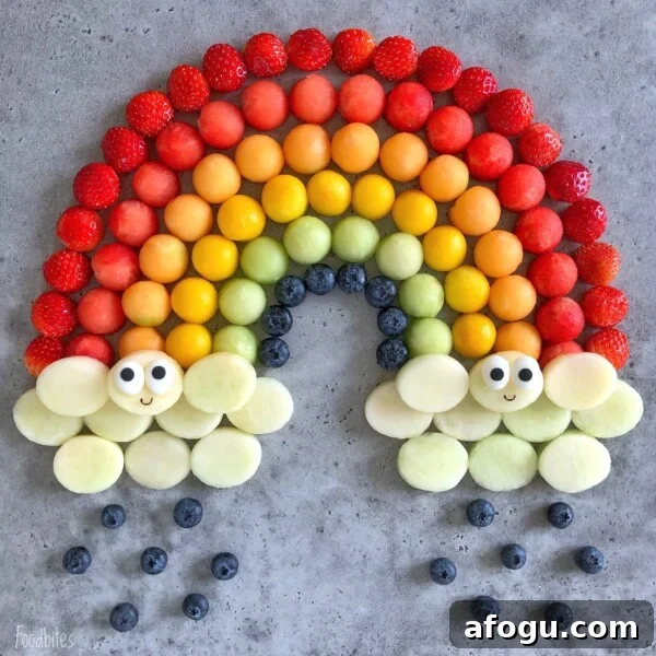 Elegant Fruit Platter Ideas for Special Occasions 4 Assorted fruit balls arranged in a rainbow pattern with strawberry, melon, and blueberry, ending in clouds made of melon with cute faces.