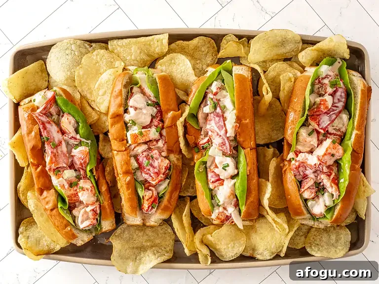 Lobster rolls with fresh lobster meat, lettuce, and tartar sauce in toasted buns, served with potato chips.