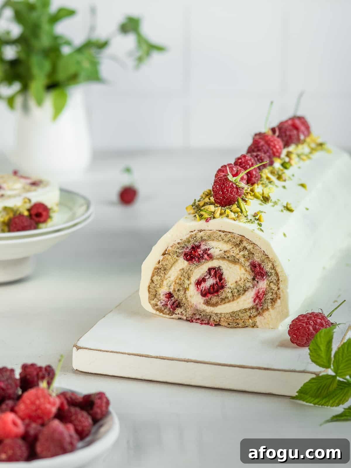 Assembled pistachio roulade on a white cake board with raspberries in the background 