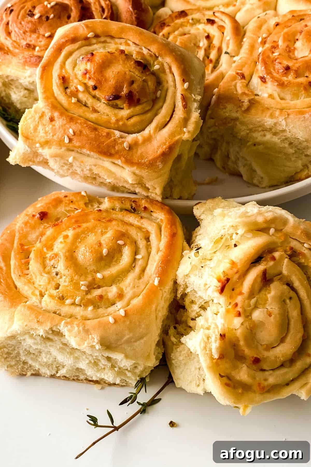 Golden brown Pull Apart Pizza Bread buns topped with sesame seeds are arranged on a white plate, with a few pieces placed in the foreground on a white surface.