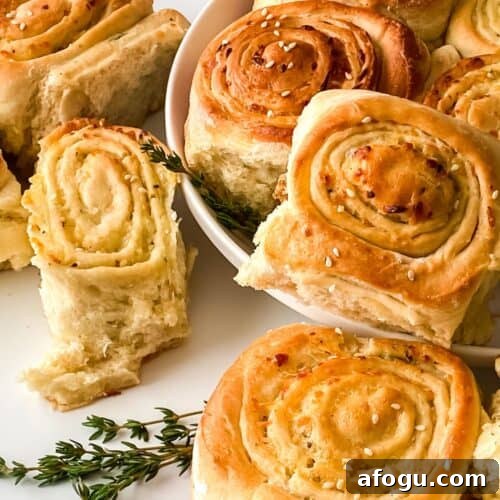 A plate of golden-brown garlic rolls, some topped with sesame seeds, arranged with a few sprigs of fresh herbs on a white surface, evokes the tempting look of Pull Apart Pizza Bread.