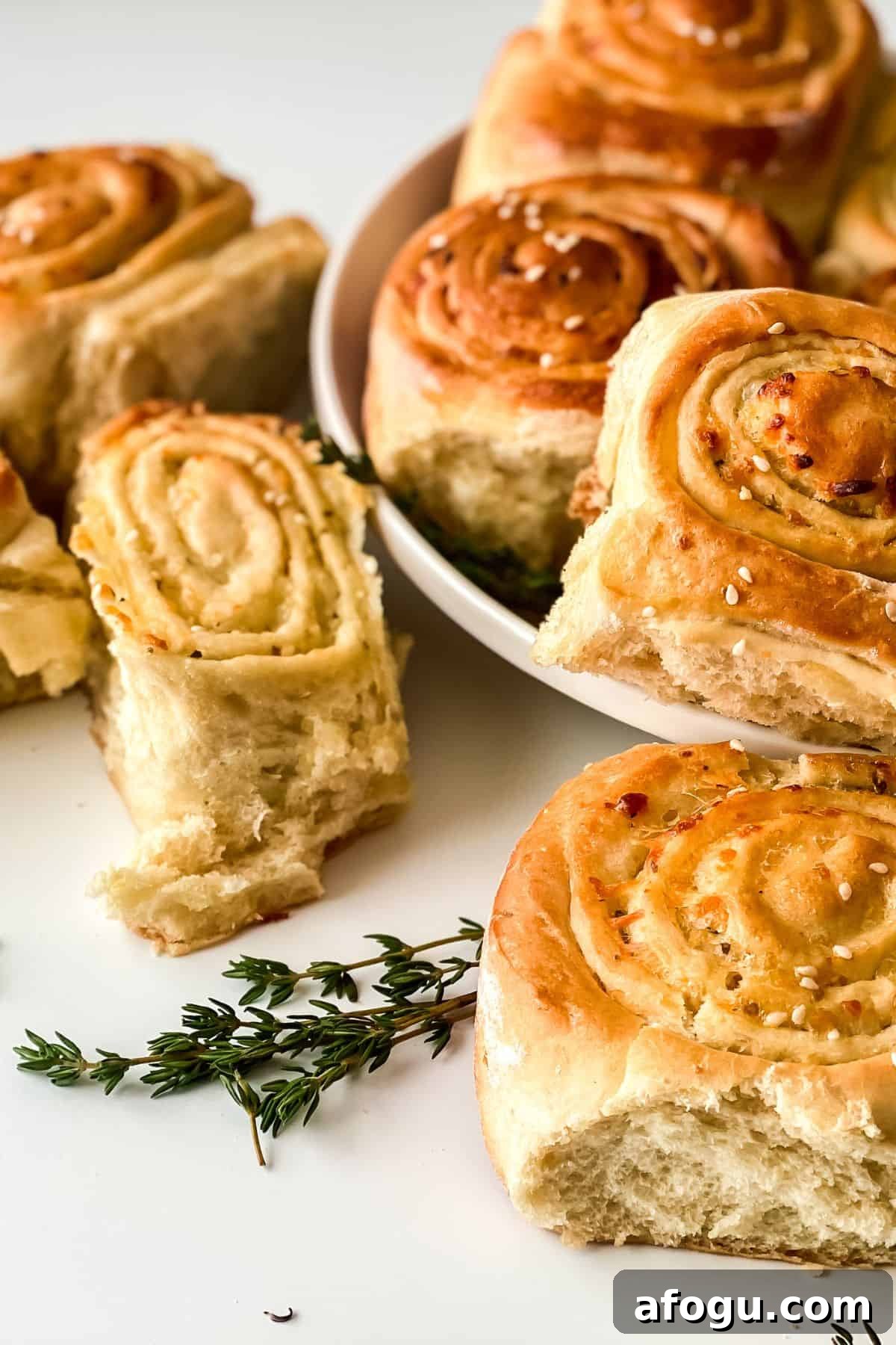 Golden brown, spiral-shaped Pull Apart Pizza Bread rolls with sesame seeds on top, arranged on a white plate and surface, garnished with fresh thyme.