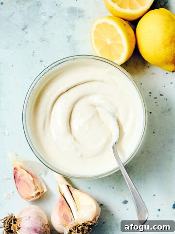 Creamy Shawarma sauce in a bowl with a spoon, with lemons and garlic.