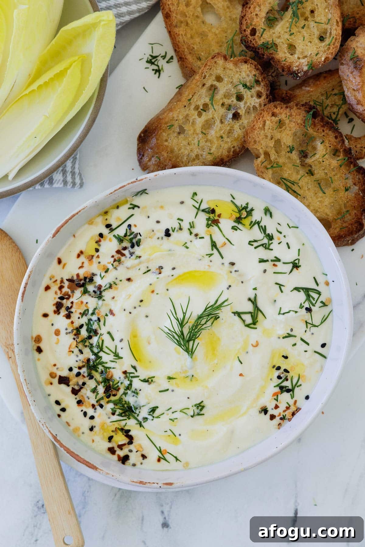 A bowl of whipped ricotta cheese with herbs, with endive leaves and crostini.