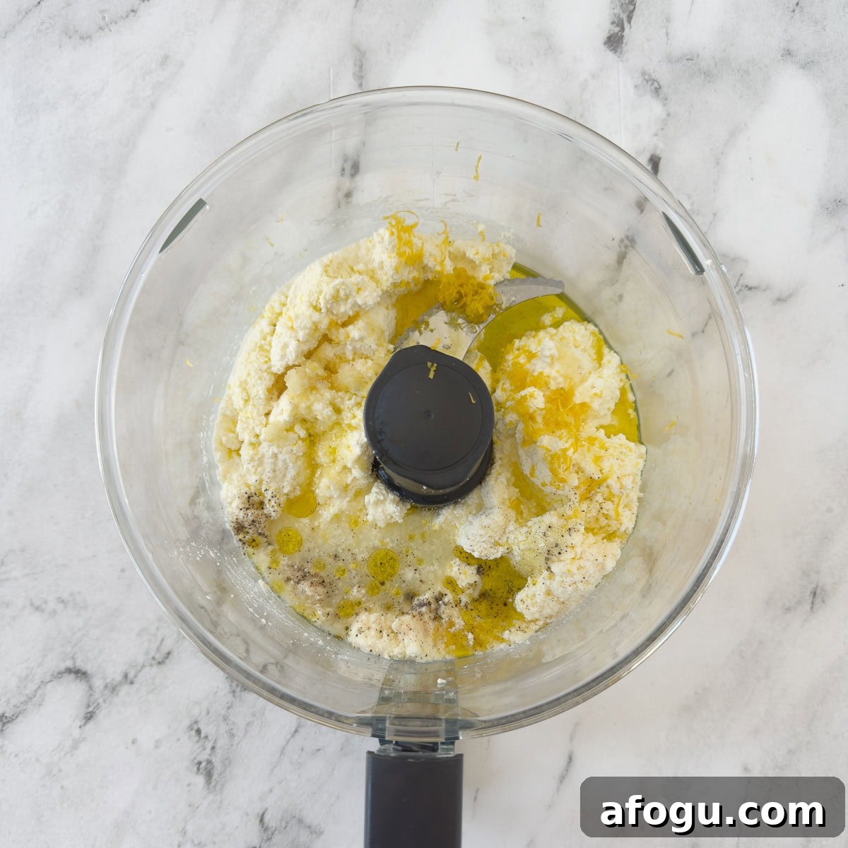 Ingredients for whipped ricotta in the bowl of a food processor. 