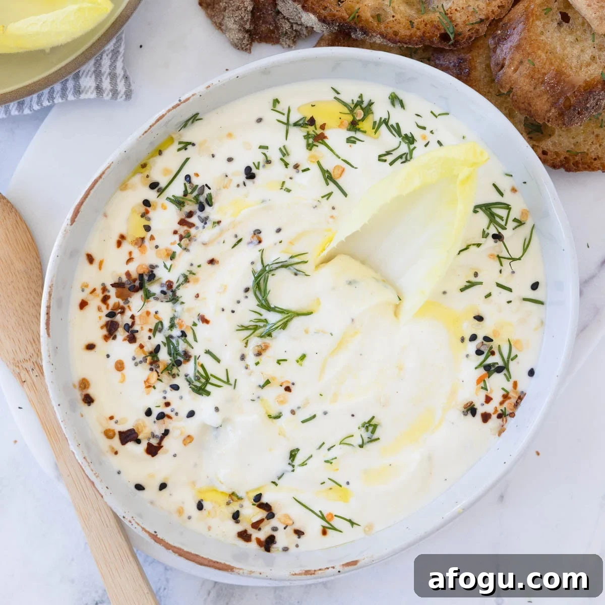 A bowl of whipped ricotta cheese dip with endive leaf in for scooping.