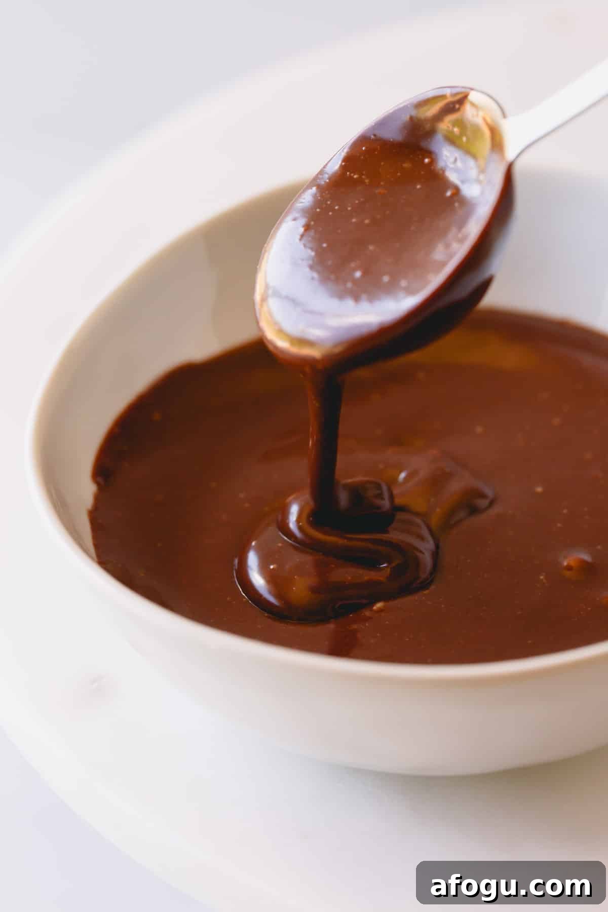 Chocolate frosting in a bowl with a spoon lifting a scoop.