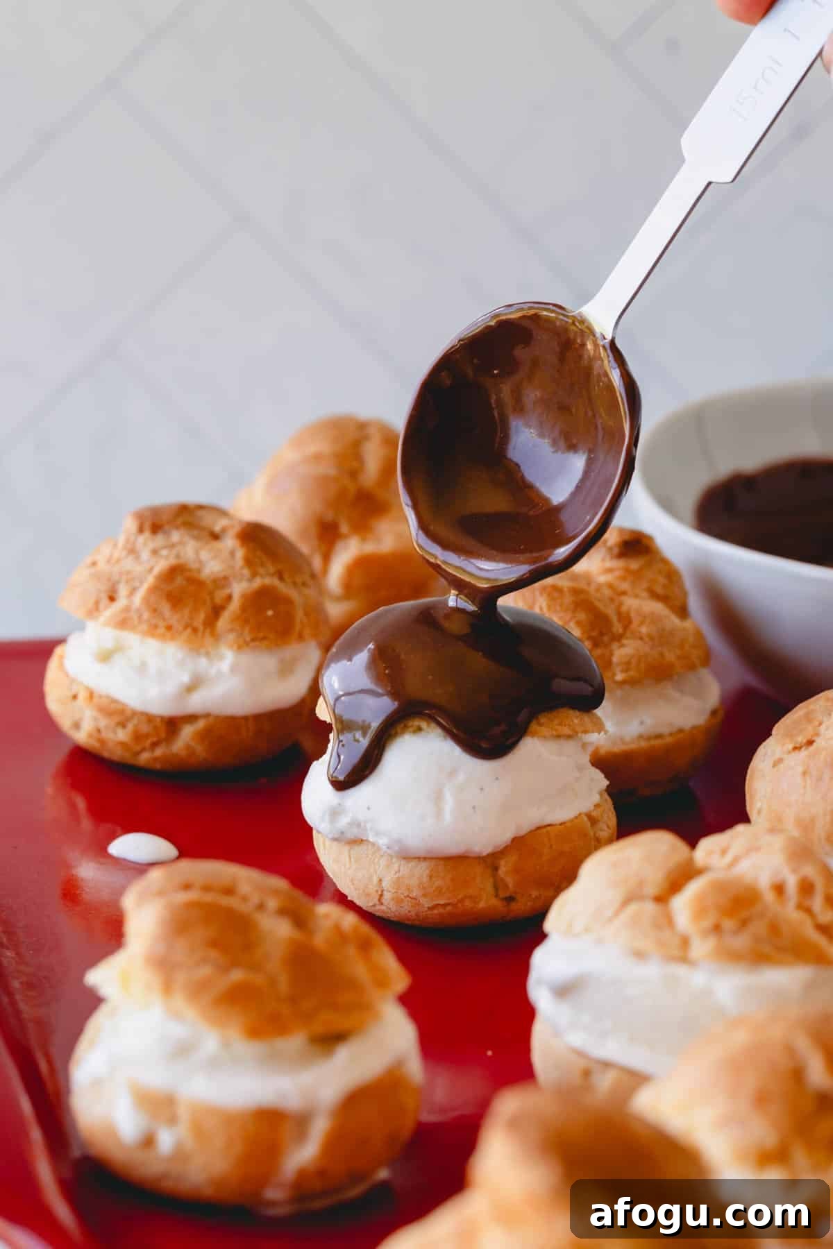 Chocolate sauce being poured over profiteroles.