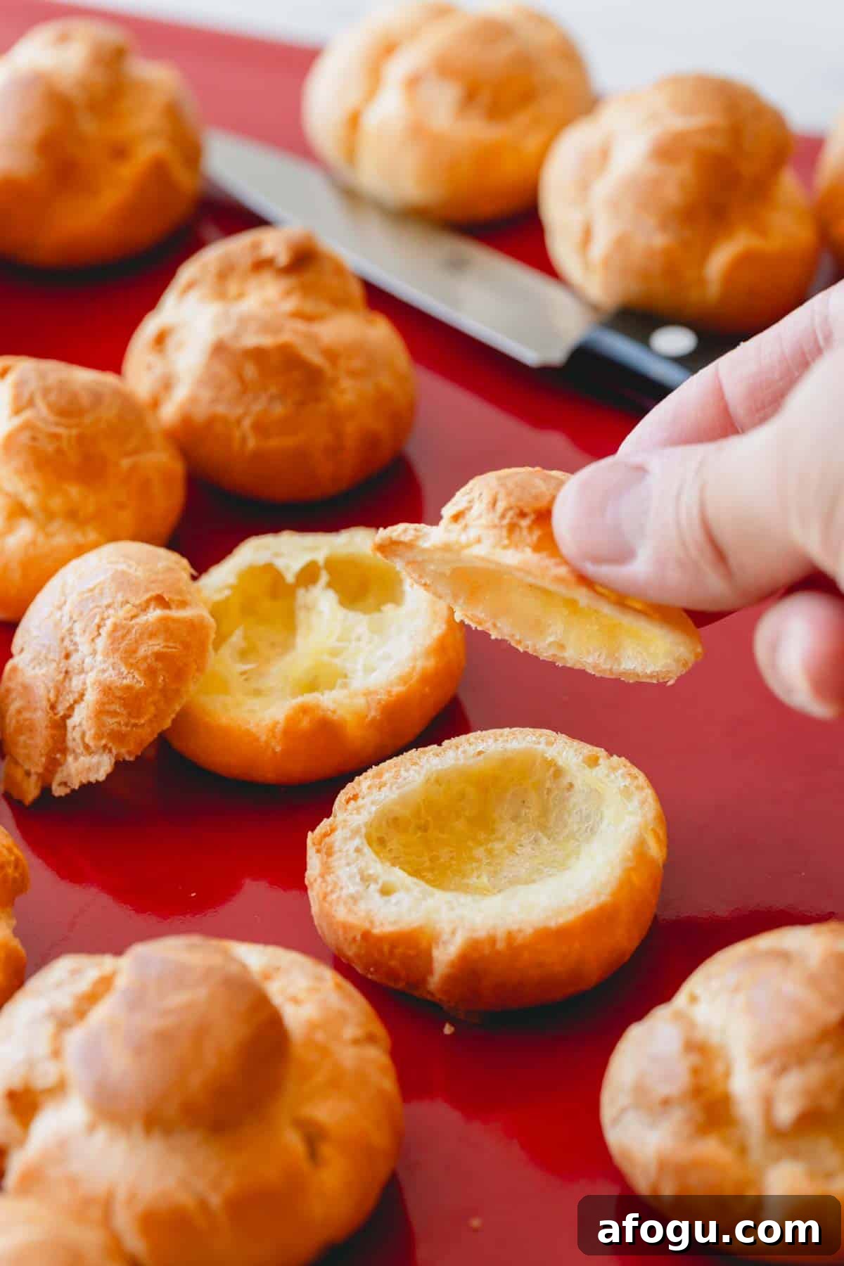 Profiteroles shells being sliced with a hand holding the top of one.