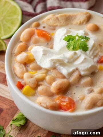 White bowl with cooked white chicken chili with cilantro and sour cream.