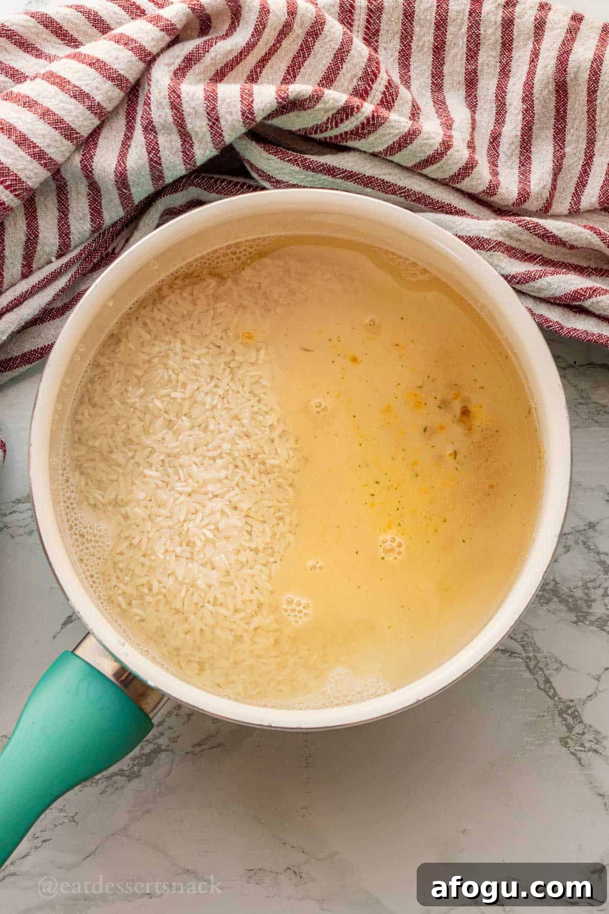 Raw rice and chicken broth in metal pot.
