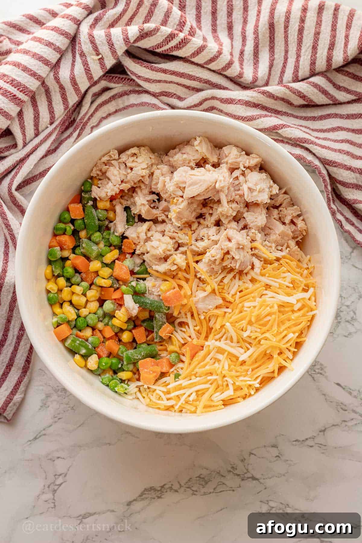 Cheese, chicken, and frozen veggies in white bowl.