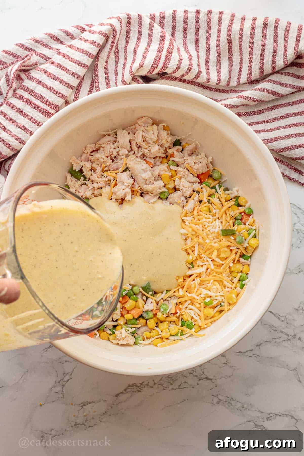 Pouring sauce into bowl of chicken, veggies, and cheese.