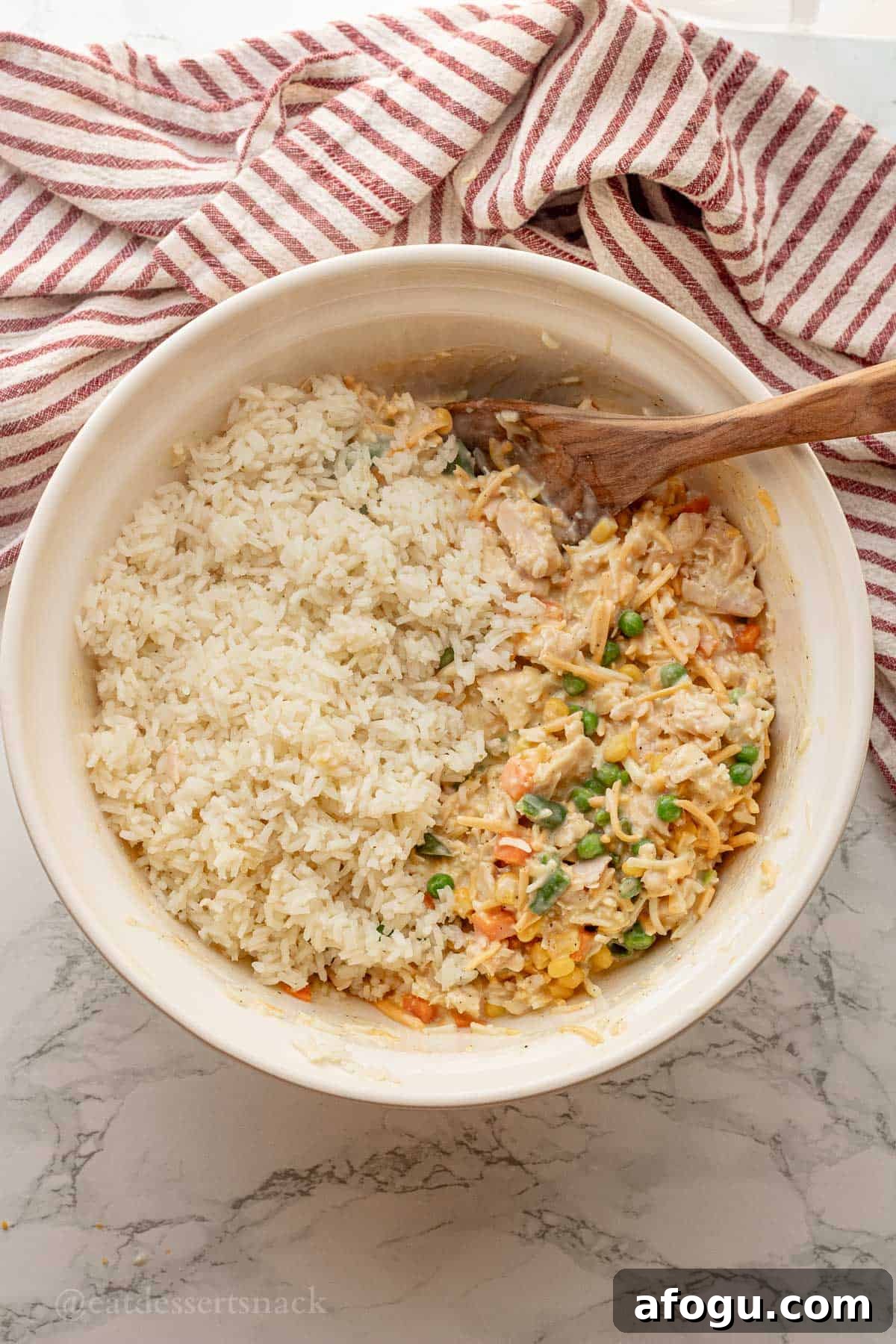 Cooked rice, veggies, and gravy in white mixing bowl with wooden spoon.