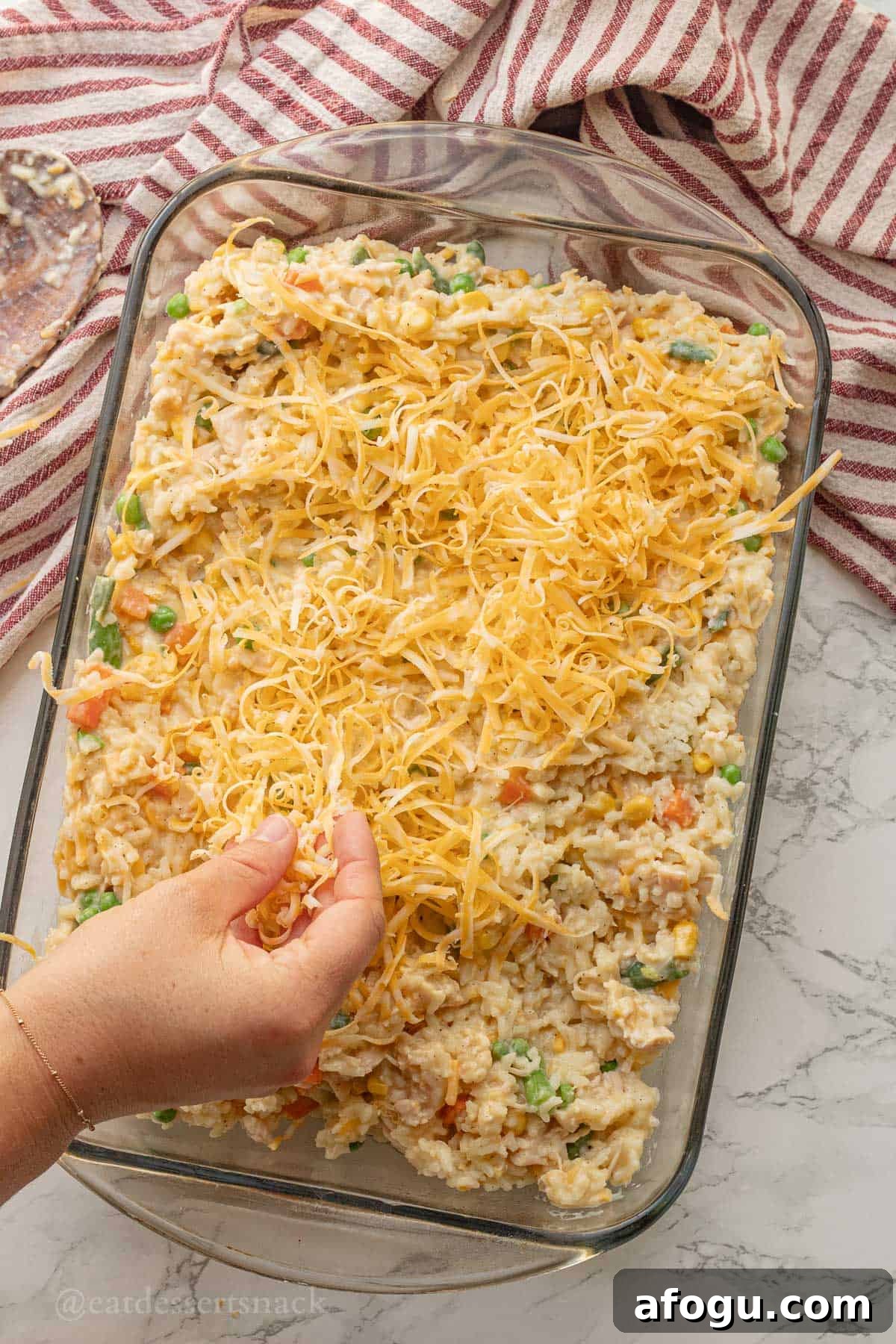 Sprinkling cheese over raw chicken and rice in glass pan.