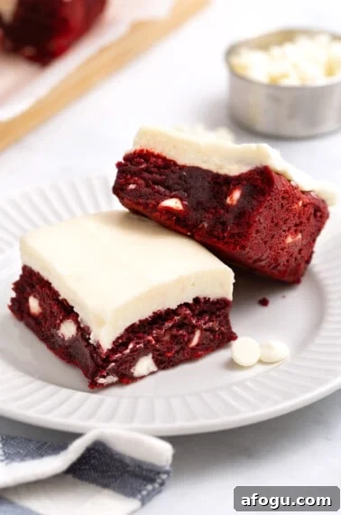 Two red velvet brownies with cream cheese frosting on a plate.