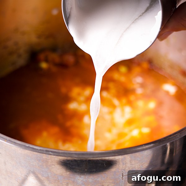 Pouring coconut milk into a pot of curried roasted coconut soup.
