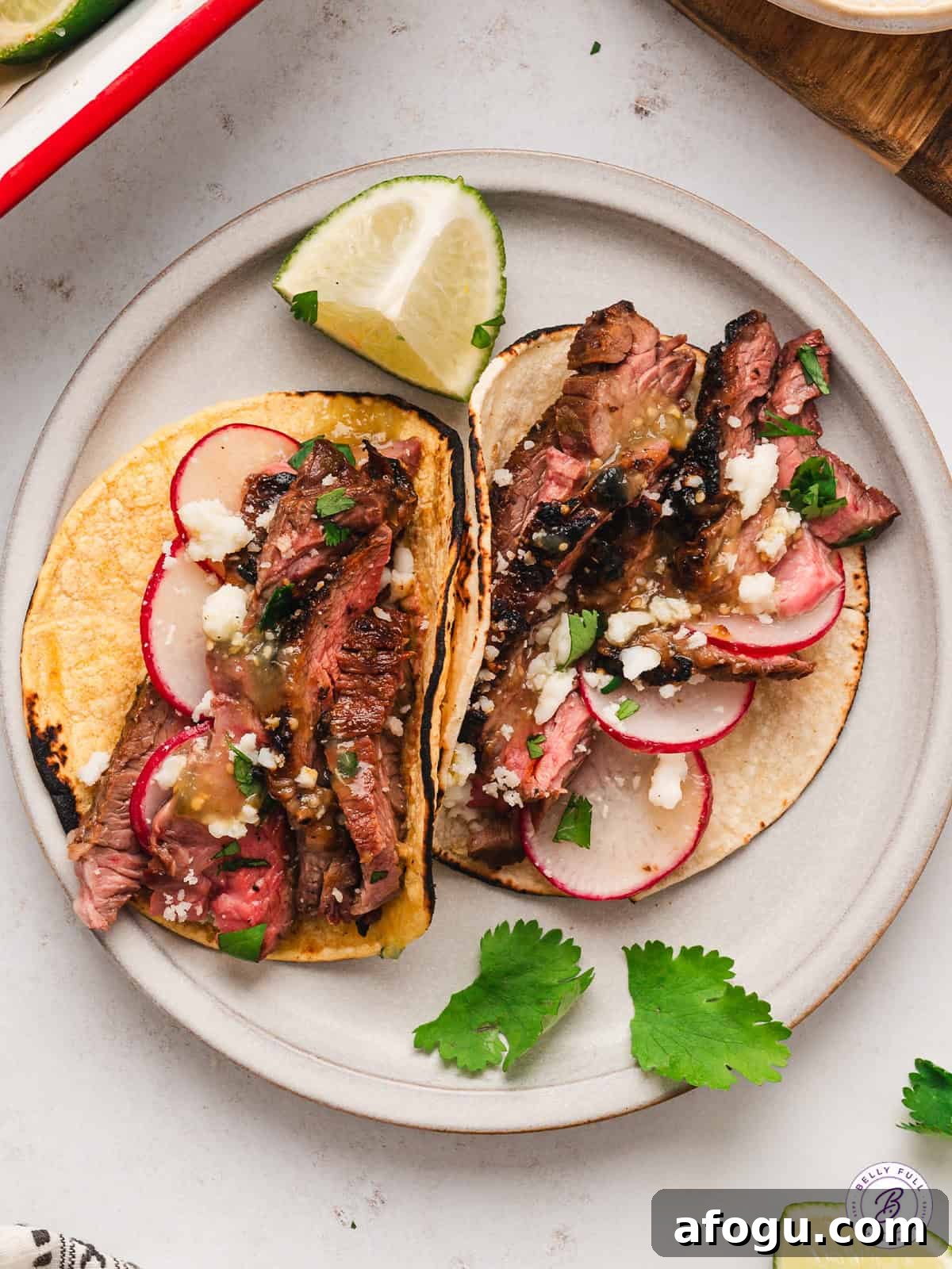 These vibrant Baja Steak Tacos are loaded with zippy marinaded grilled skirt steak and topped with cotija cheese, radishes, and cilantro. 2 Baja street tacos on a plate.