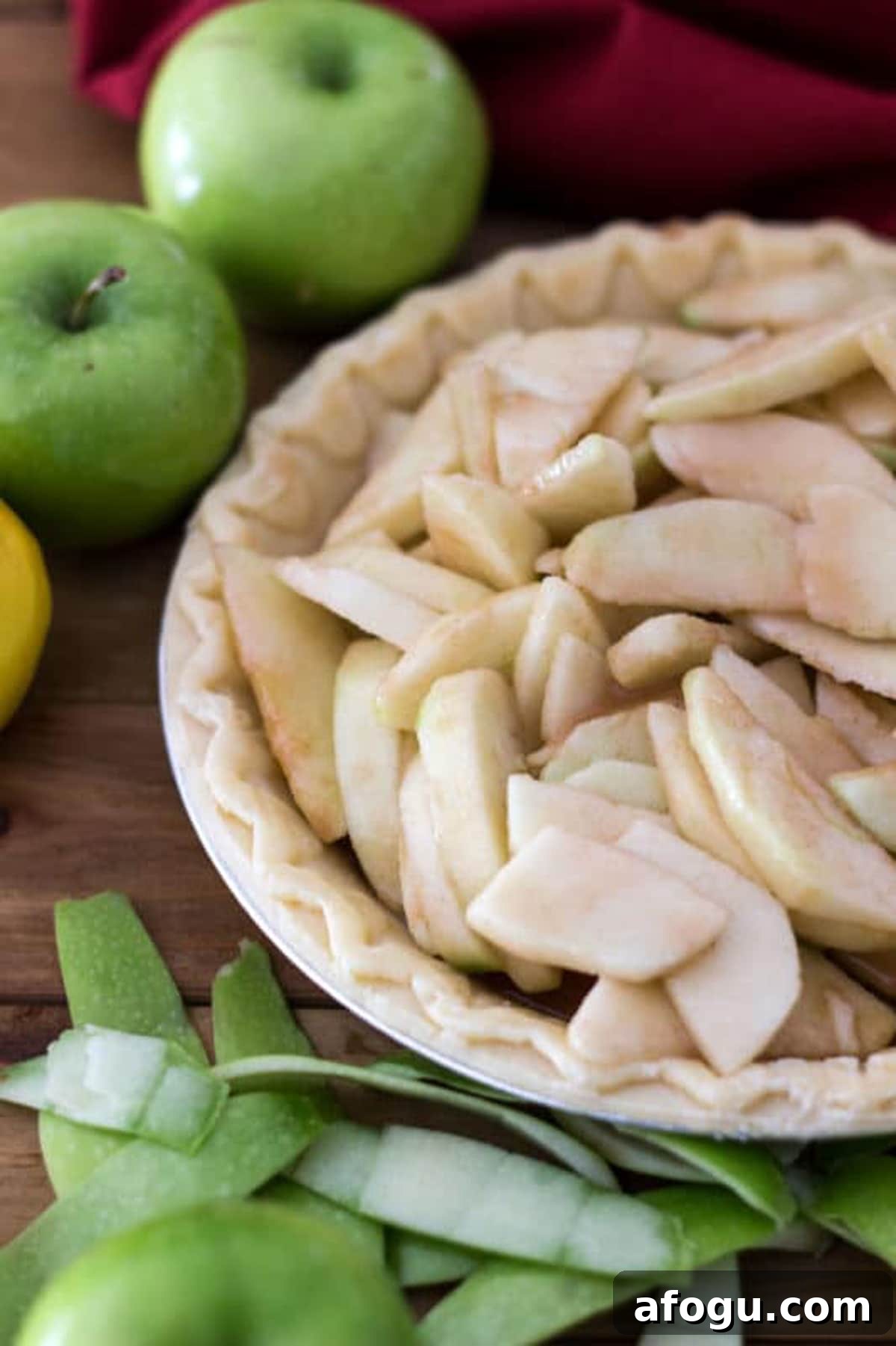 Pie shell containing apple pie filling, granny smith apples and peelings on table.