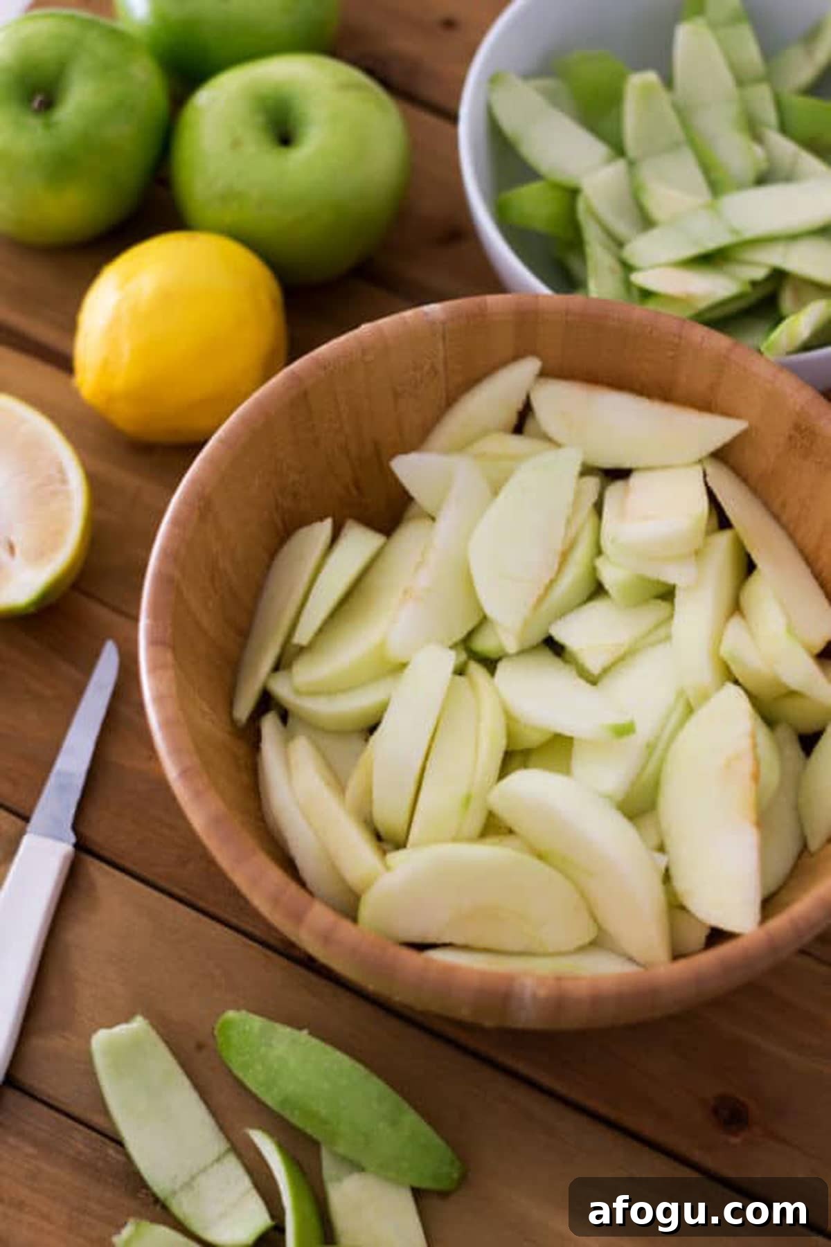 Wooden bowl containing sliced Granny Smith apples sitting on a wood table.