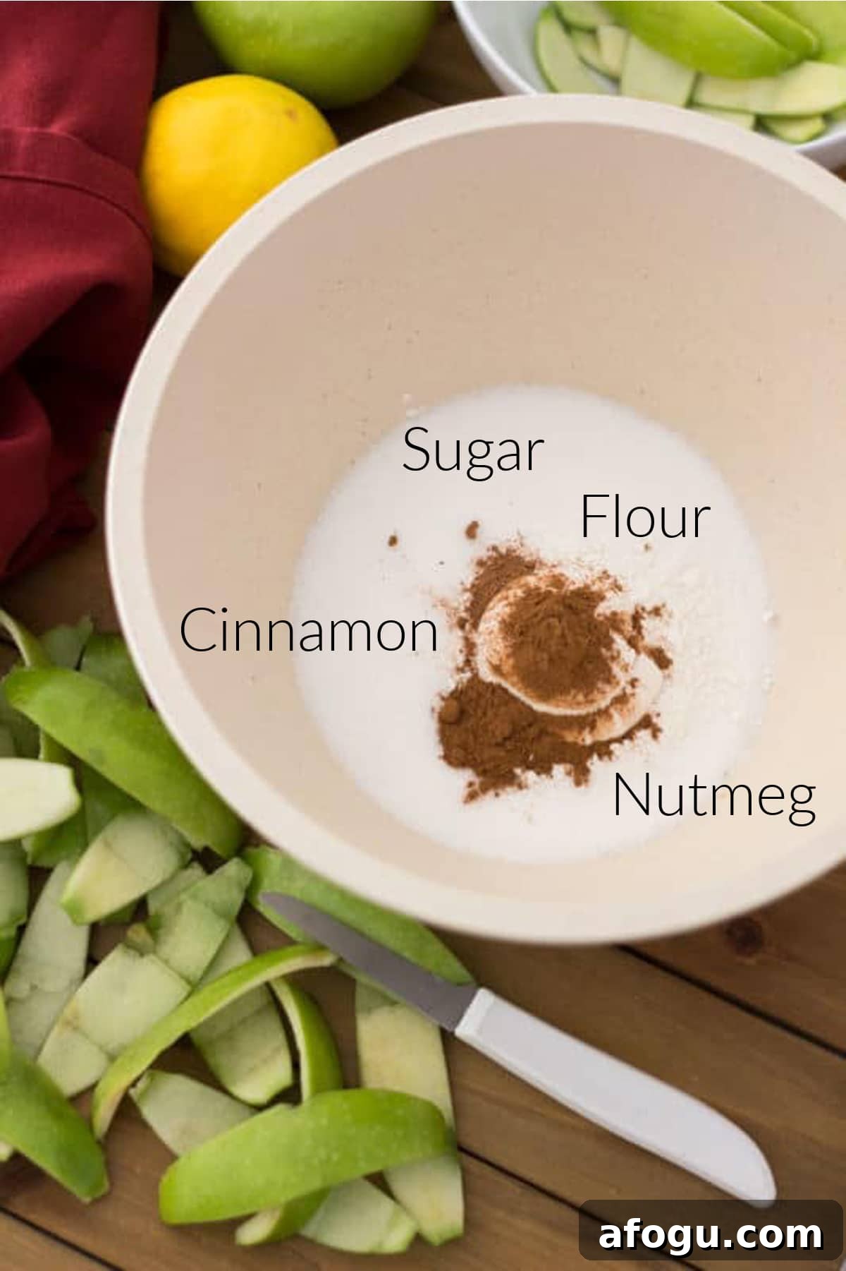 Wooden bowl containing flour, cinnamon, nutmeg and flour, granny smith apple peelings on table.