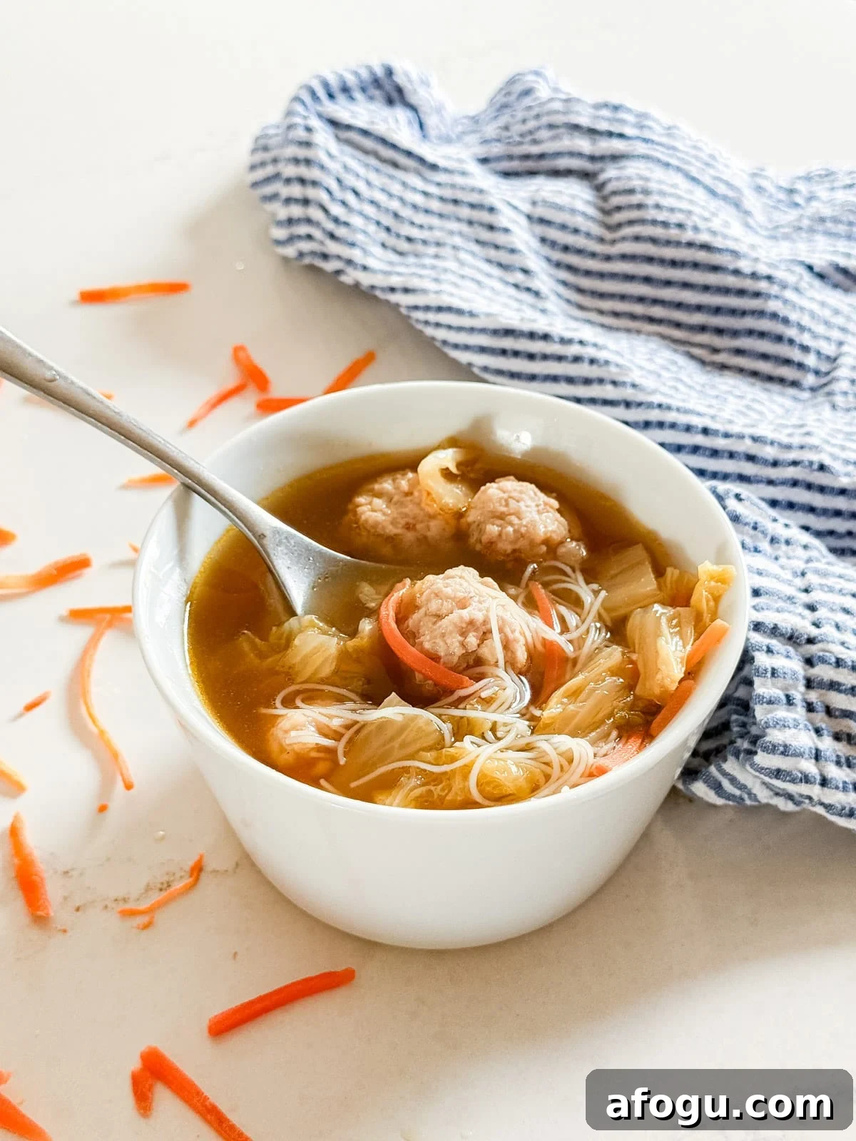 Asian Cabbage and Pork Meatball Soup Recipe 2 A bowl of asian soup with meatballs with a spoon and noodles in it.