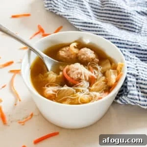 Asian Cabbage and Pork Meatball Soup Recipe 15 A bowl of asian soup with meatballs with a spoon and noodles in it.