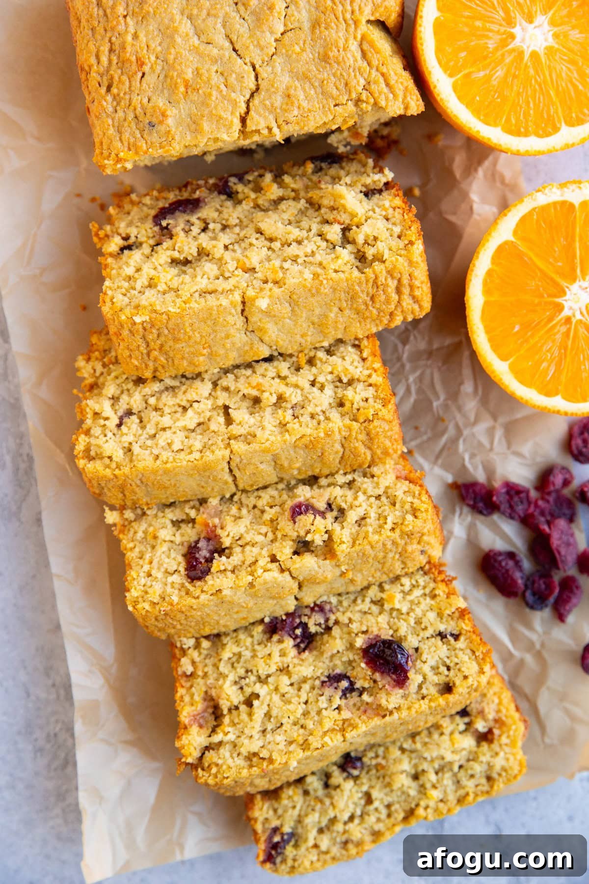 Loaf of cranberry orange bread cut into slices with a halved orange next to the bread and some dried cranberries.