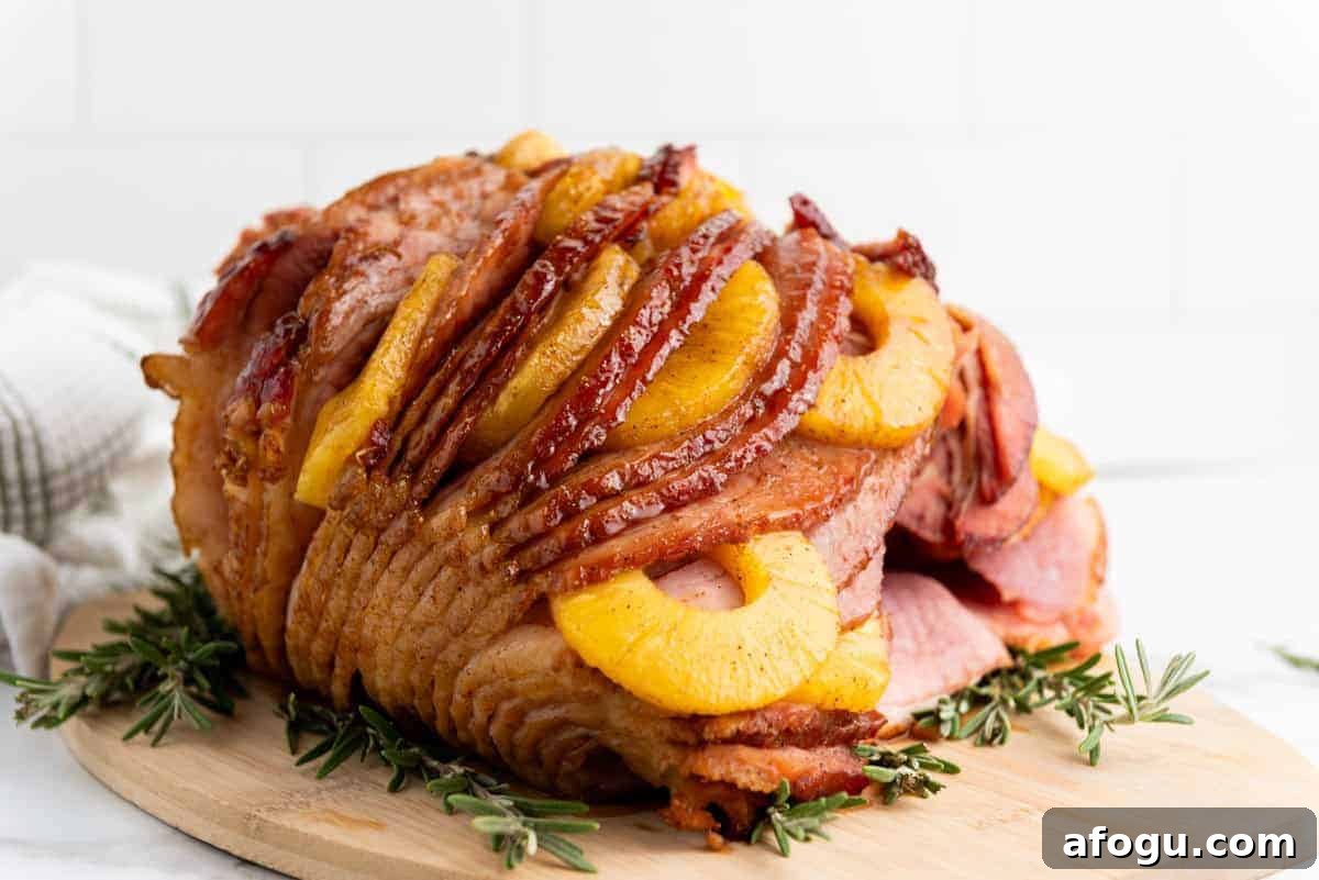 A Brown Sugar Pineapple Ham is placed on a wooden board, garnished with sprigs of rosemary.