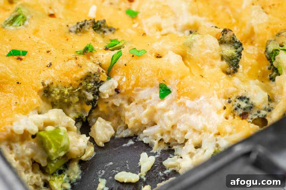 Close-up of a cheesy broccoli and rice casserole in a baking dish, with a serving removed, showing melted cheese, rice, broccoli, and garnished parsley.