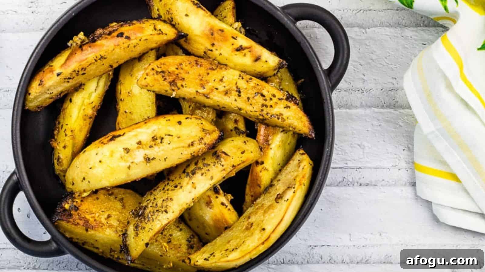Round black dish filled with seasoned roasted potato wedges, placed on a white wooden surface alongside a white and yellow striped cloth napkin.