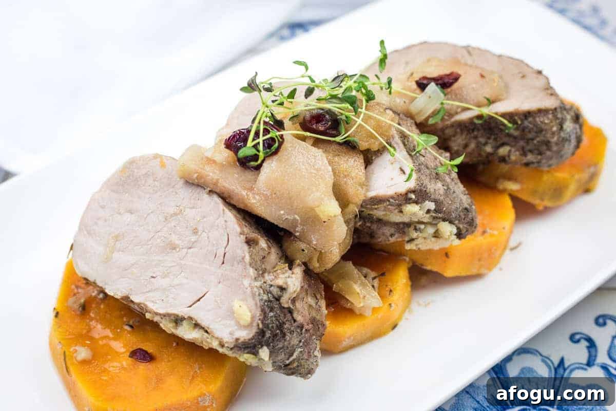 Sliced slow cooker pork roast with sweet potatoes & apples on a white plate.