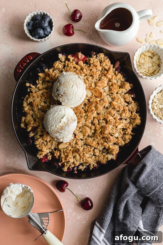 Overhead view of a cherry almond crisp in a cast iron pan with scoops of ice cream on top.